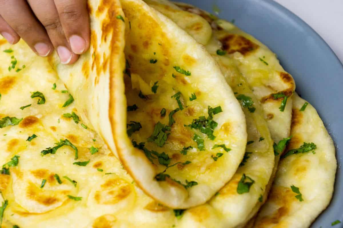 Close-up of cheesy naan flatbread topped with fresh herbs, golden-brown spots, in a light blue dish.