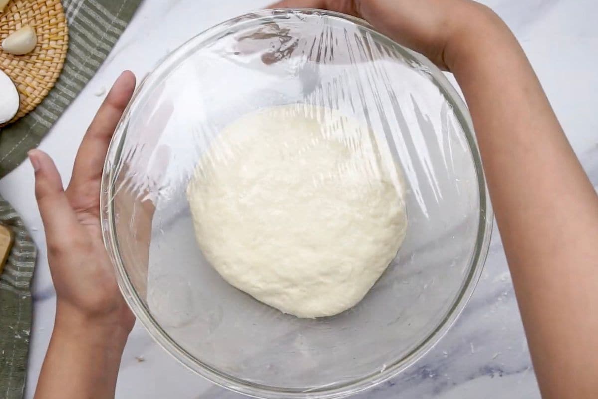 Soft, freshly made bread dough covered with plastic wrap, ready to rise.
