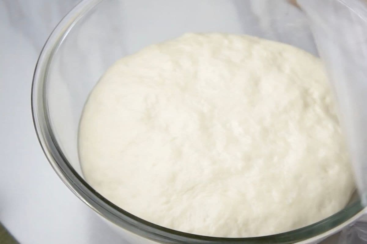 Soft, risen pizza dough in a clear glass bowl, ready for baking.