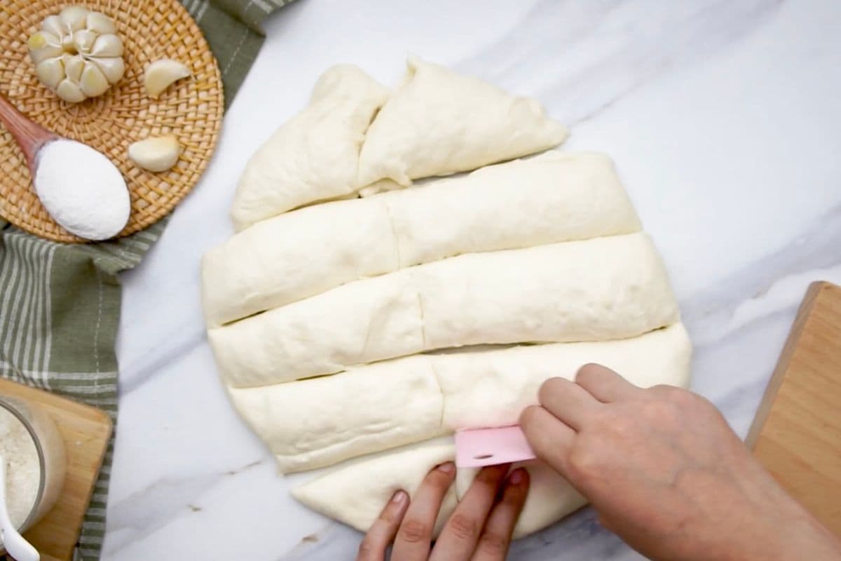 Alt: Preparing dough triangles on a marble surface with garlic and flour nearby.