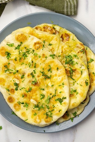Delicious homemade garlic naan with melted cheese garnished with fresh herbs, perfect for any meal.