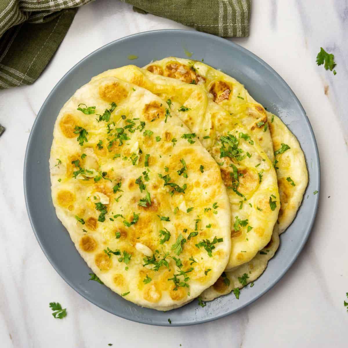 Delicious homemade garlic naan with melted cheese garnished with fresh herbs, perfect for any meal.