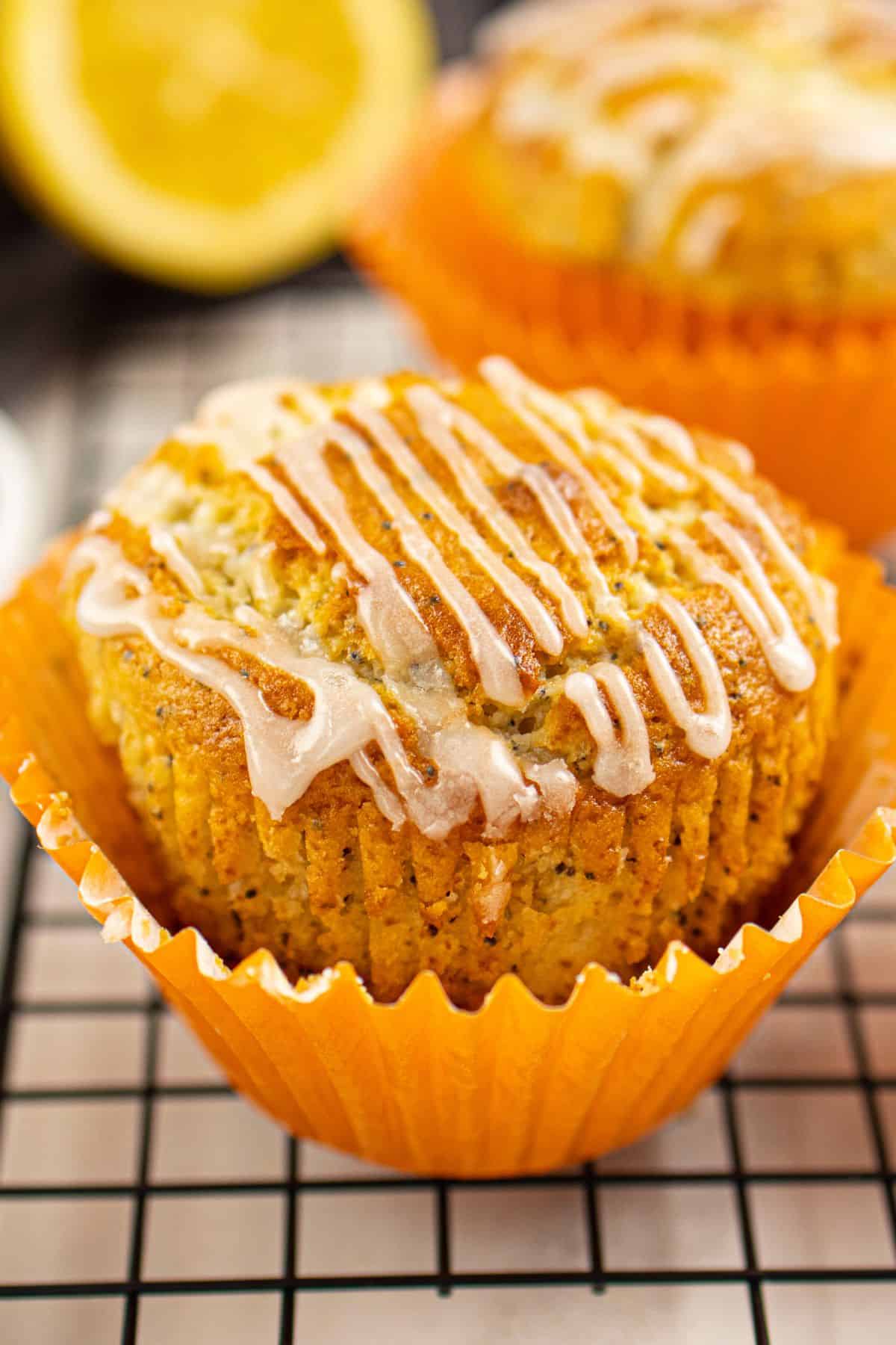 A close-up of a moist, homemade carrot cake muffin topped with cream cheese icing and orange paper liner.