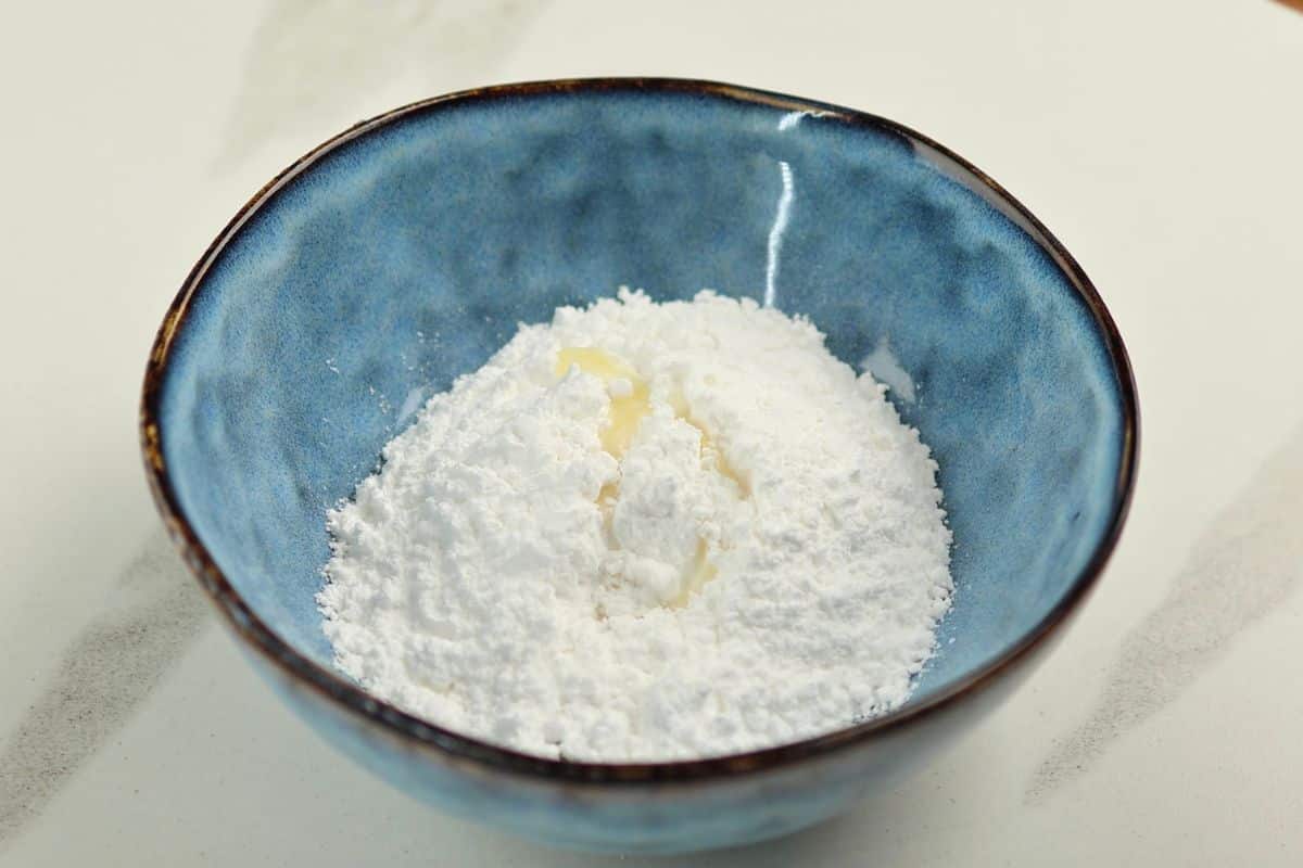 Close-up of flour with a dollop of butter in a blue ceramic bowl on white surface.