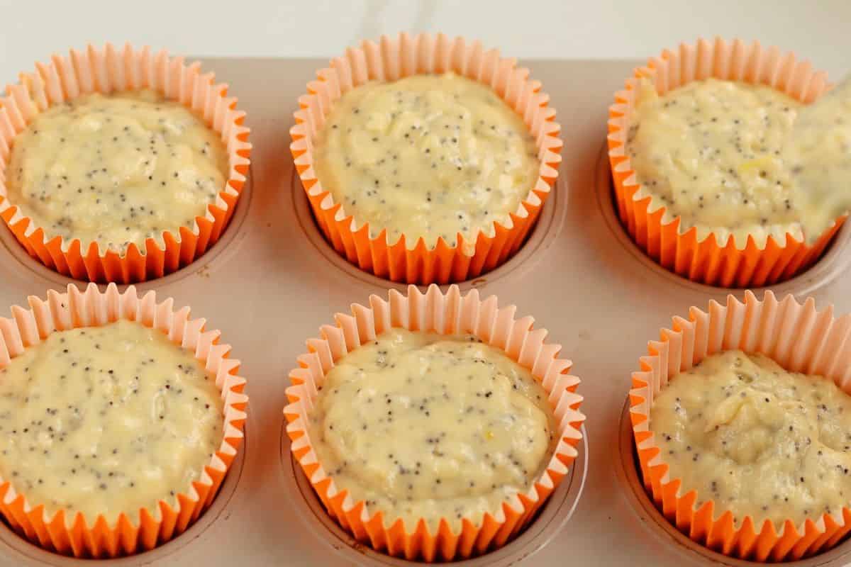Delicious cupcake batter with poppy seeds in orange paper cups before baking.