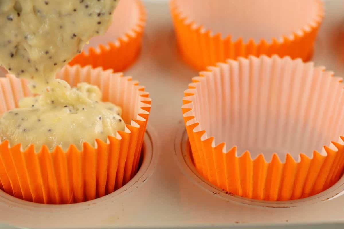 Baking cupcakes with orange liners filled with batter in a muffin tin.