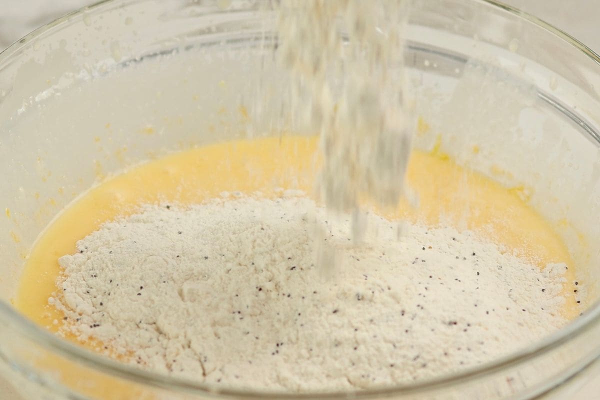 A close-up of flour being added to a mixing bowl with cake batter, ready for baking.