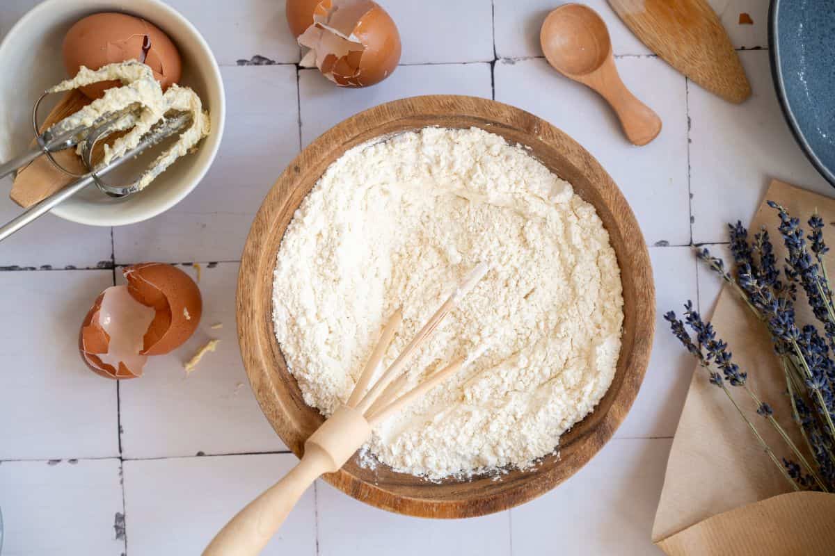 Fresh flour mixture in a wooden bowl with baking utensils and ingredients around.