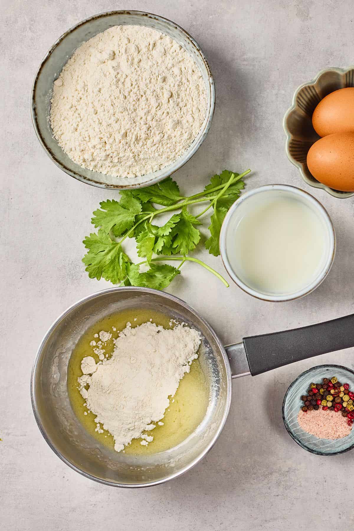 A bowl of flour, eggs, milk, cilantro, and spices ready for baking or cooking.