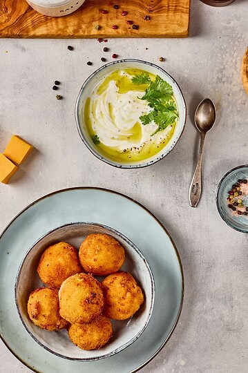 Delicious cheese balls served with creamy dip, fresh herbs, and colorful seasonings on a modern table.