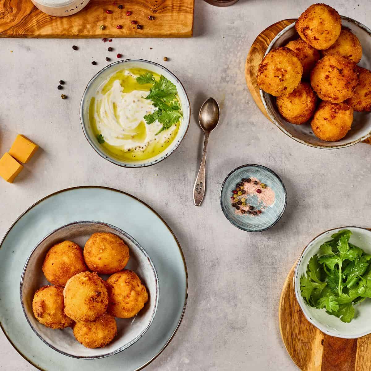 Delicious cheese balls served with creamy dip, fresh herbs, and colorful seasonings on a modern table.