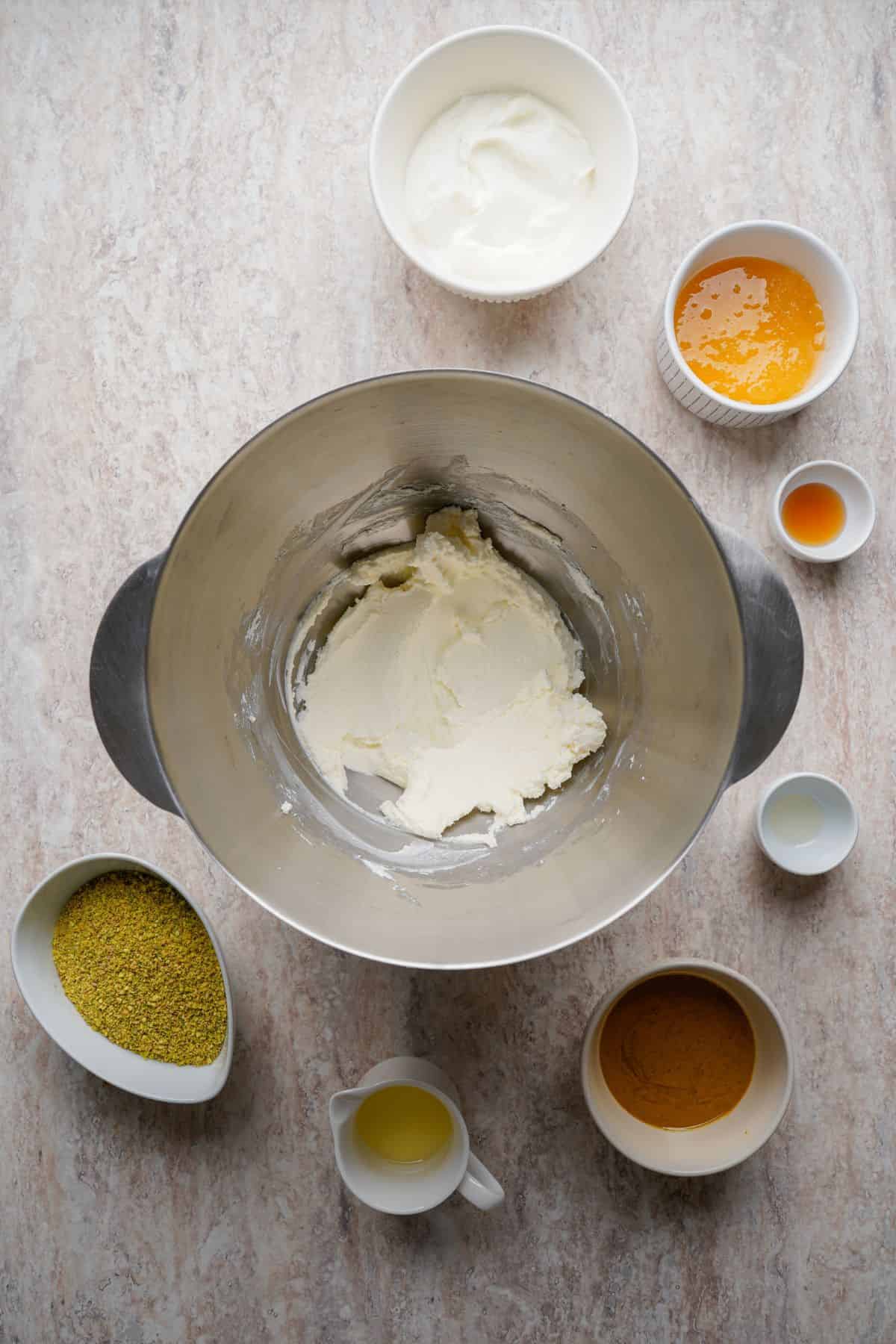 Cream cheese in mixing bowl with various ingredients around it.