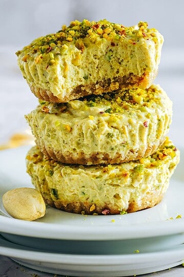 Delicious pistachio cheesecake with chopped nuts on top, served on a white plate. An indulgent dessert option.