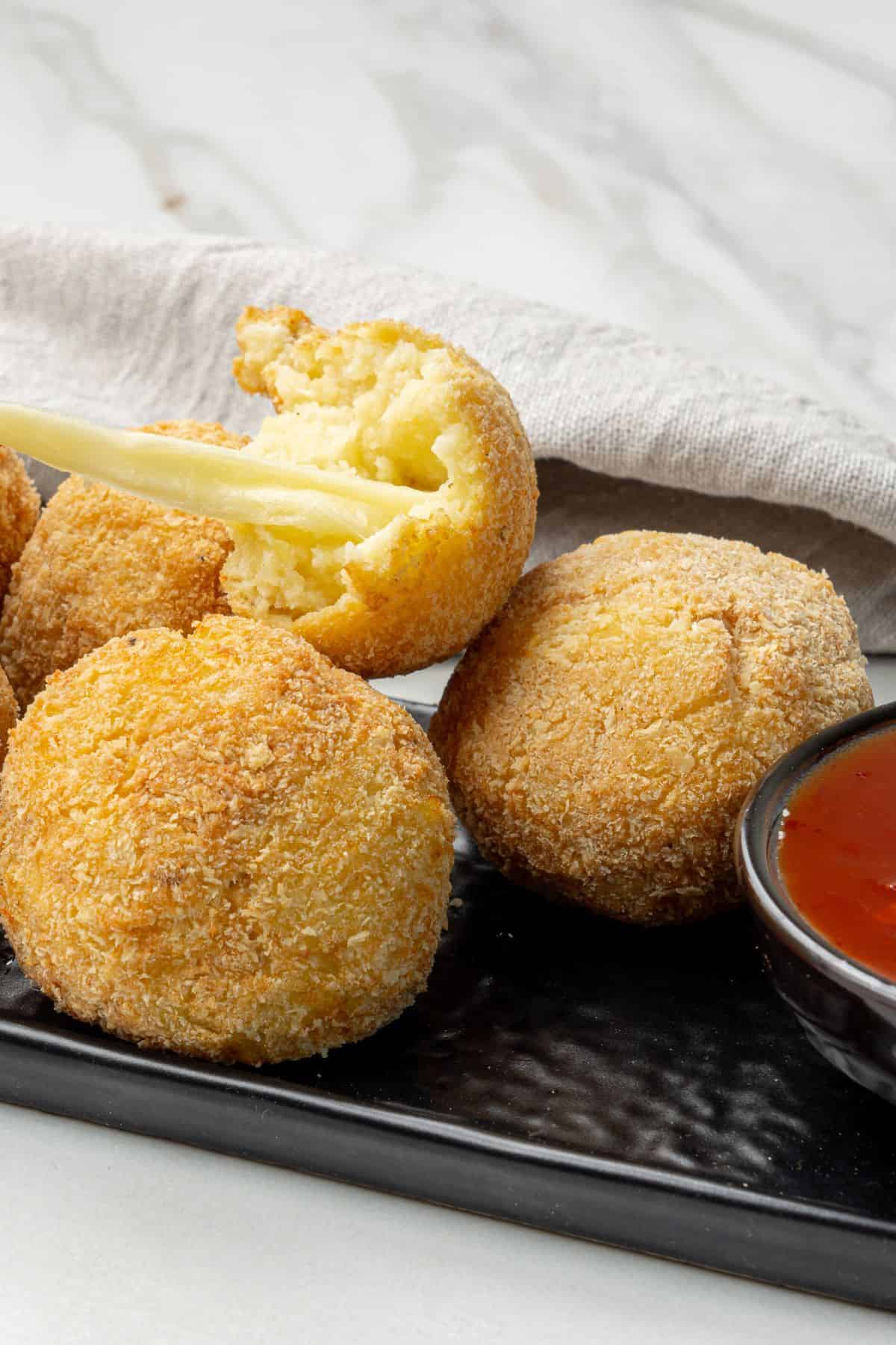 Delicious crispy cheese balls served with spicy dipping sauce on a black platter.
