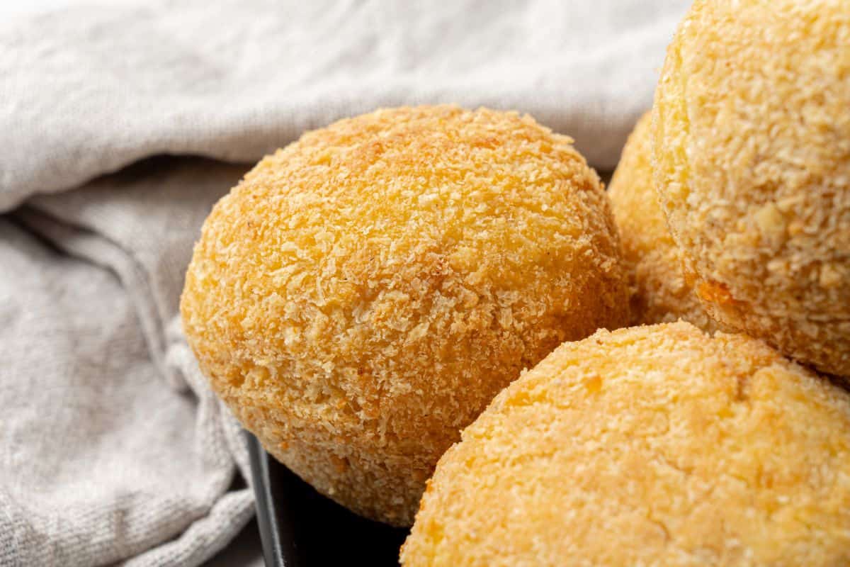 Close-up of crispy, golden cheese balls on a black plate.