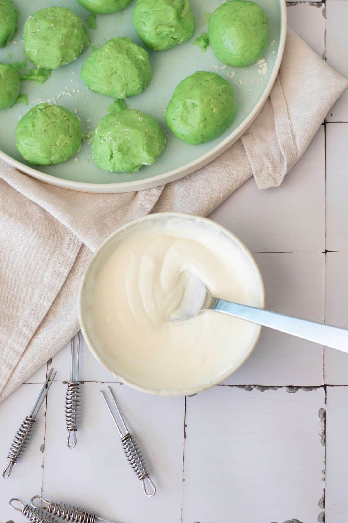 Delicious green dough balls ready for baking with creamy white icing in a bowl.