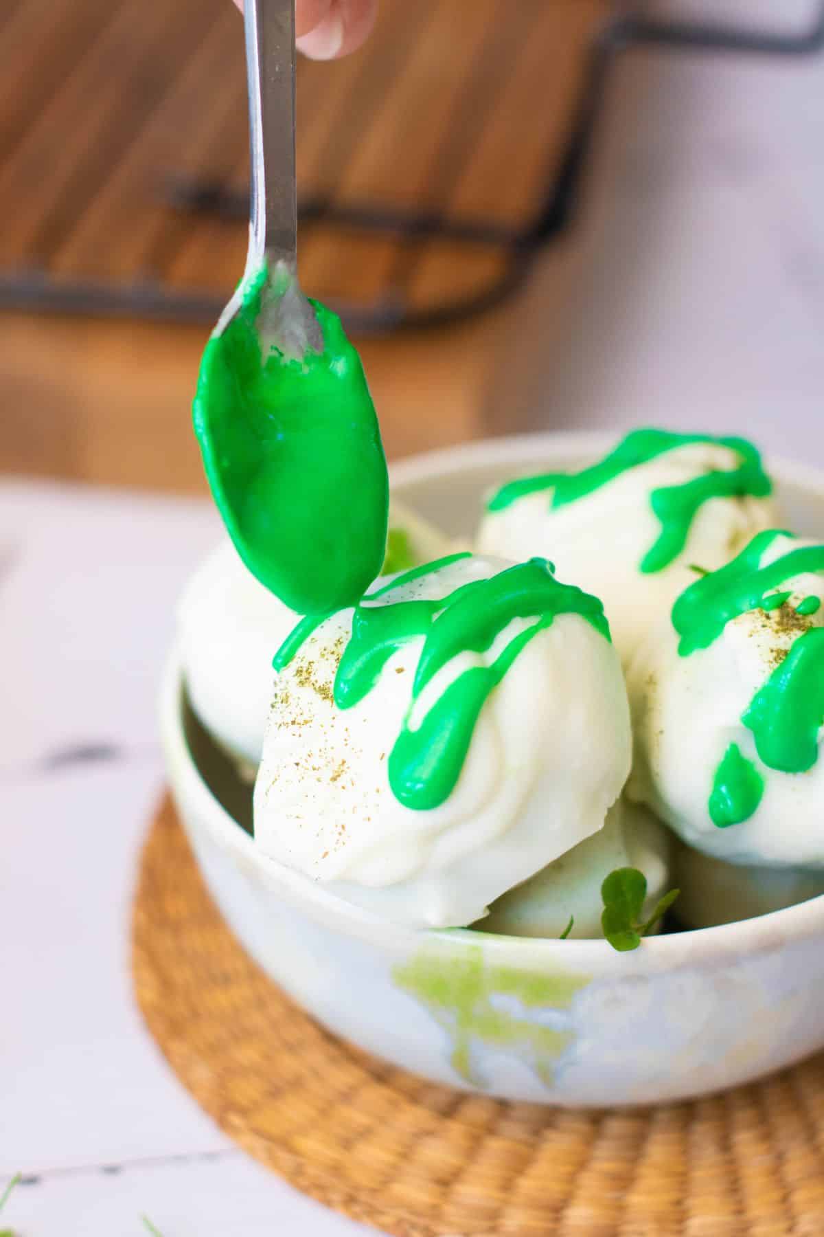 Close-up of creamy vanilla ice cream scoops topped with bright green syrup, served in a white bowl.