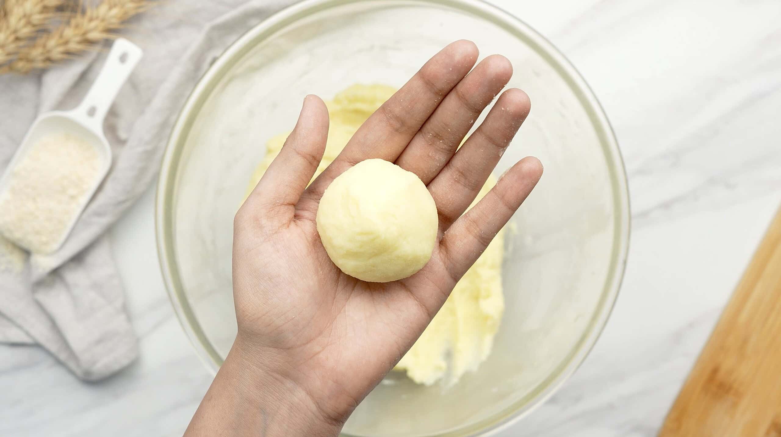Hand holding a potato ball over mixing bowl preparing homemade mashed potatoes or potato snacks.