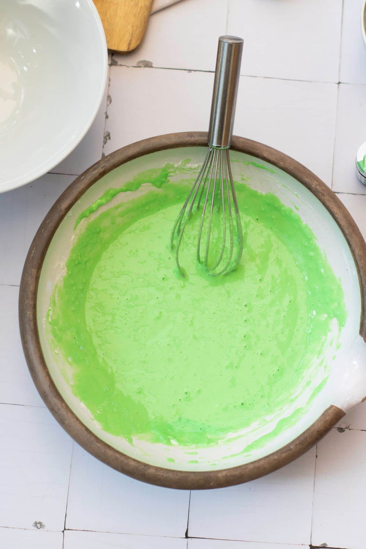 Vibrant green cake batter prepared in a bowl with a whisk, ready for baking or decorating.