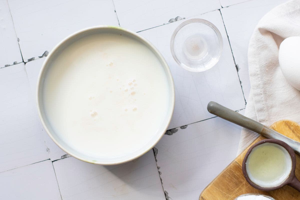 A bowl of milk with a glass of water and egg on a kitchen counter.