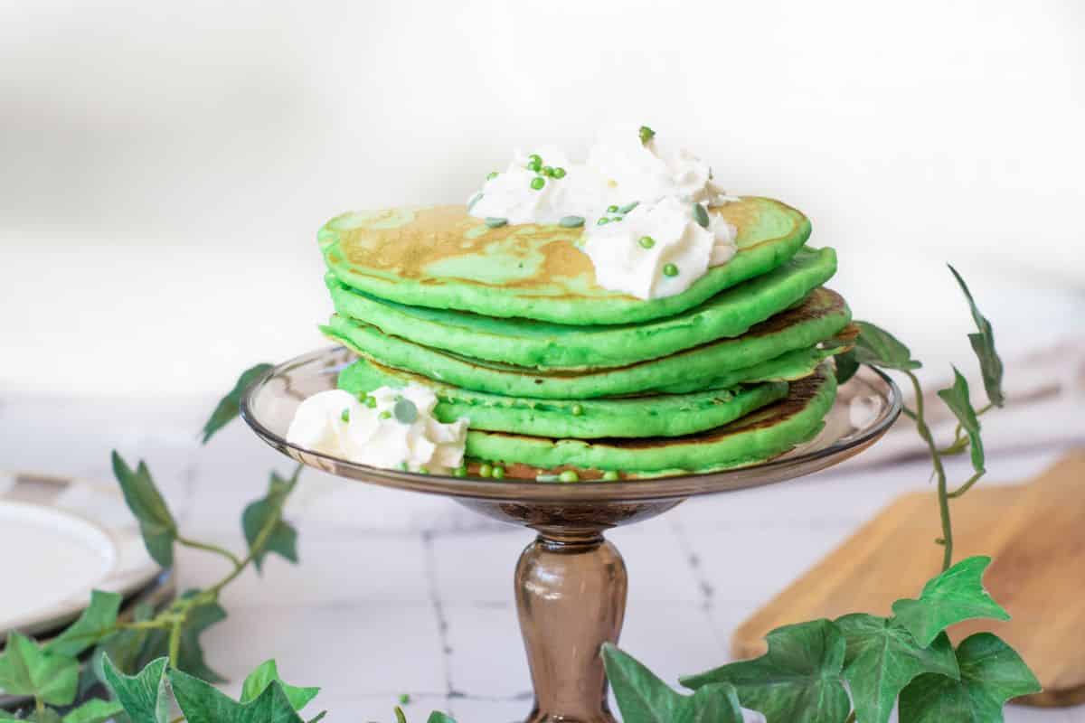 Delicious green pancakes topped with whipped cream and sprinkles, perfect for celebrating St. Patrick's Day.
