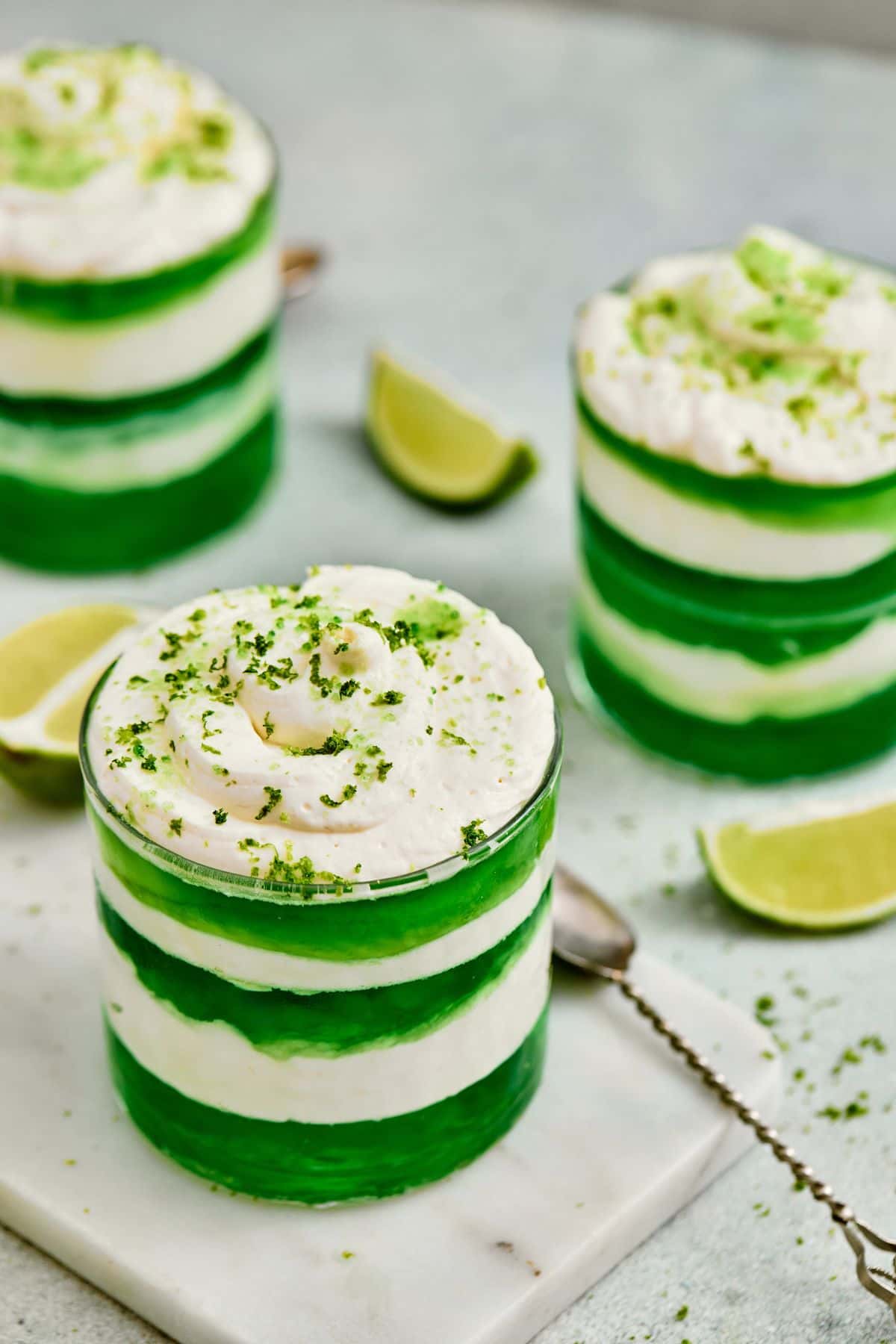 Fresh lime and vanilla layered dessert with whipped topping, vibrant green stripes, garnished with lime zest.