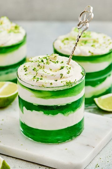 Refreshing layered lime beverage topped with whipped cream, lime zest, and a metal stirrer.