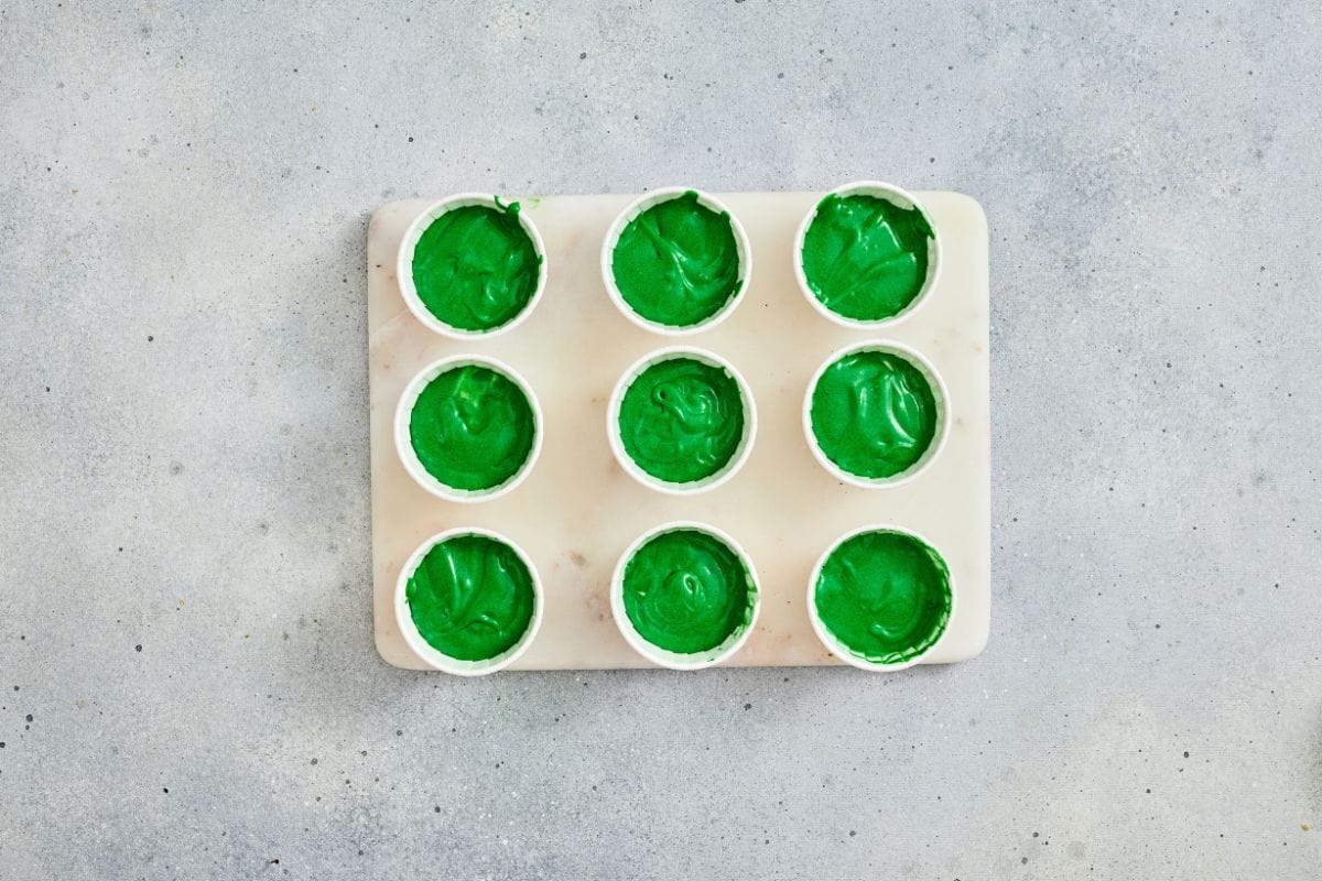 Bright green ice cubes in a white tray for drinks or parties, set on a simple gray surface.