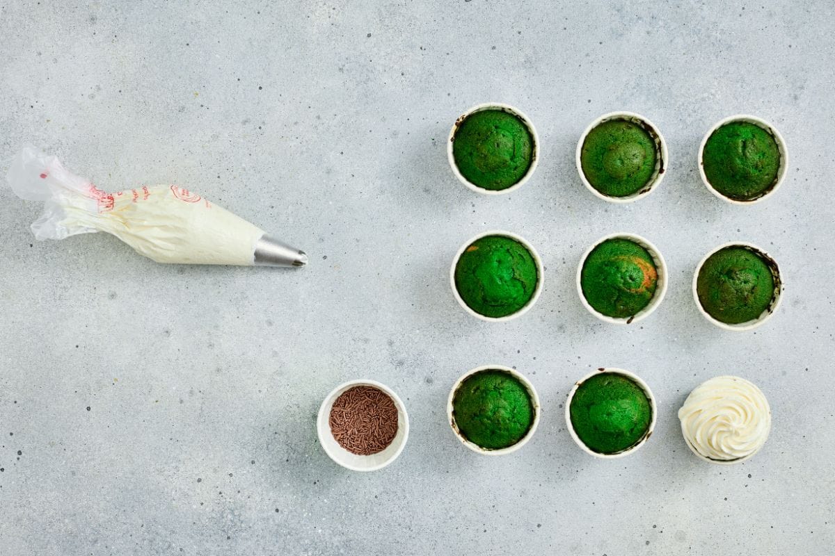 Delicious green cupcakes topped with whipped cream, sprinkles, and colorful frosting on a textured gray surface.