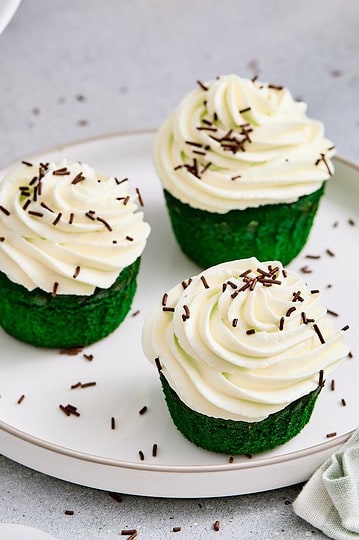 Delicious cupcakes topped with white frosting and chocolate sprinkles, served on a white plate.