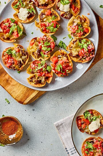 Delicious mini taco cups topped with tomatoes, cheese, and cilantro served on a gray plate. Perfect appetizer for gatherings.