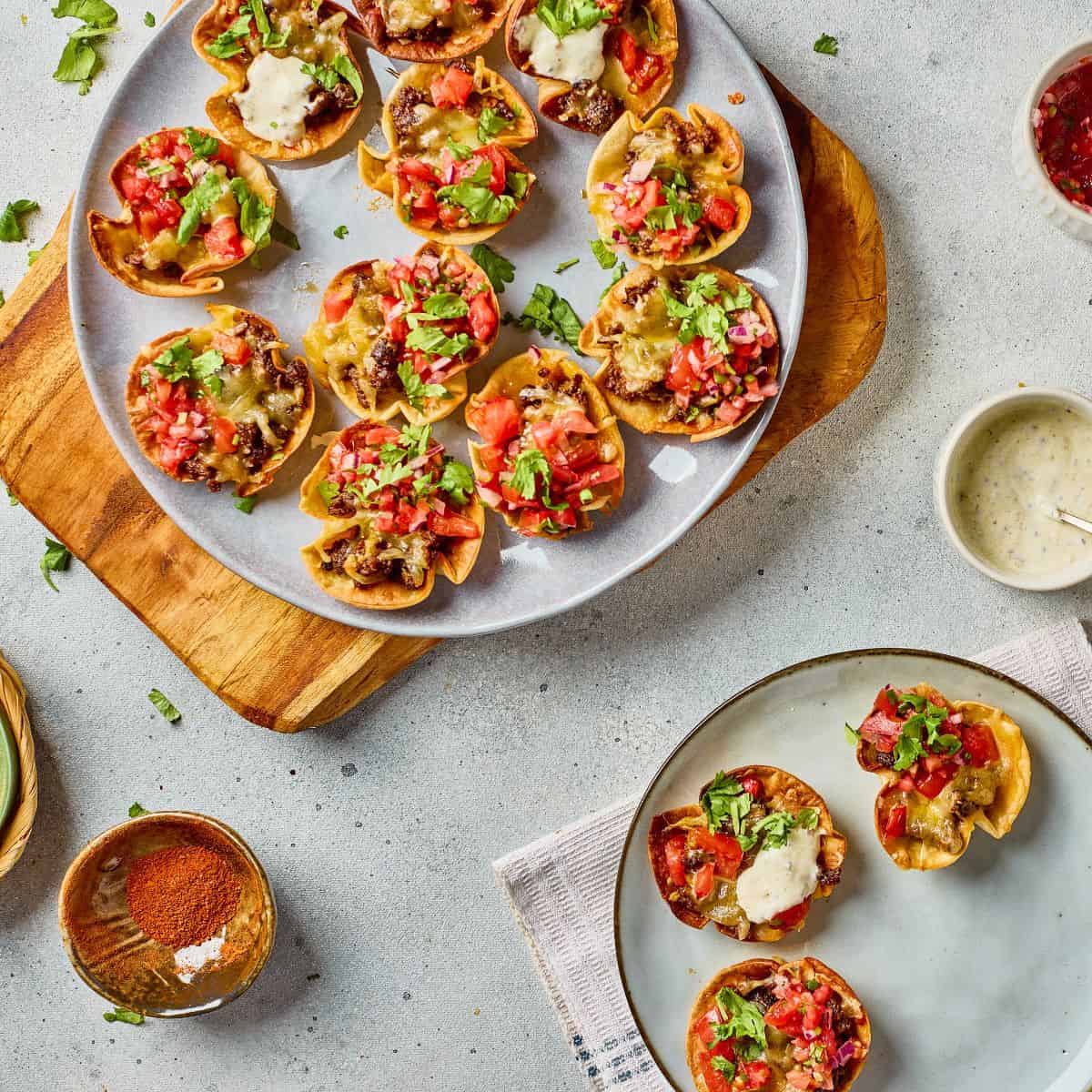 Delicious mini taco cups topped with tomatoes, cheese, and cilantro served on a gray plate. Perfect appetizer for gatherings.