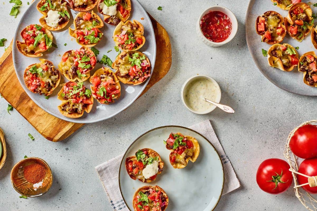 Delicious mini taco bites topped with fresh tomatoes, cheese, and herbs served on a stylish gray platter.