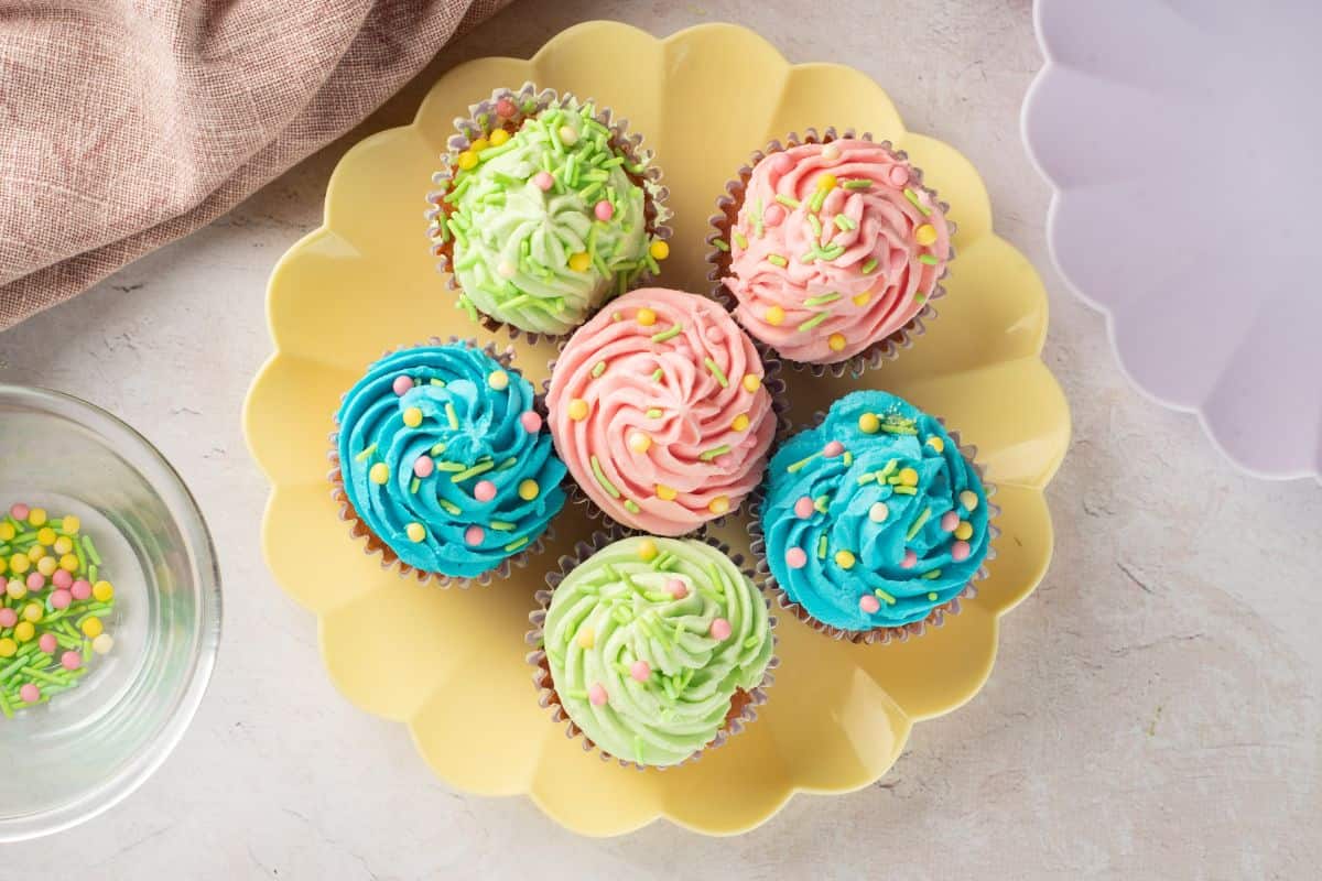 Vibrant cupcakes with pink, green, and blue frosting, decorated with sprinkles, on a yellow plate.