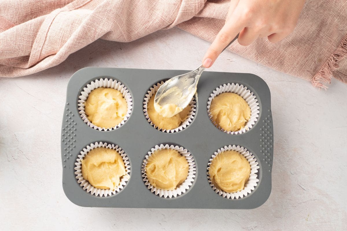 Delicious muffin batter being spooned into cupcake liners in a baking tray.