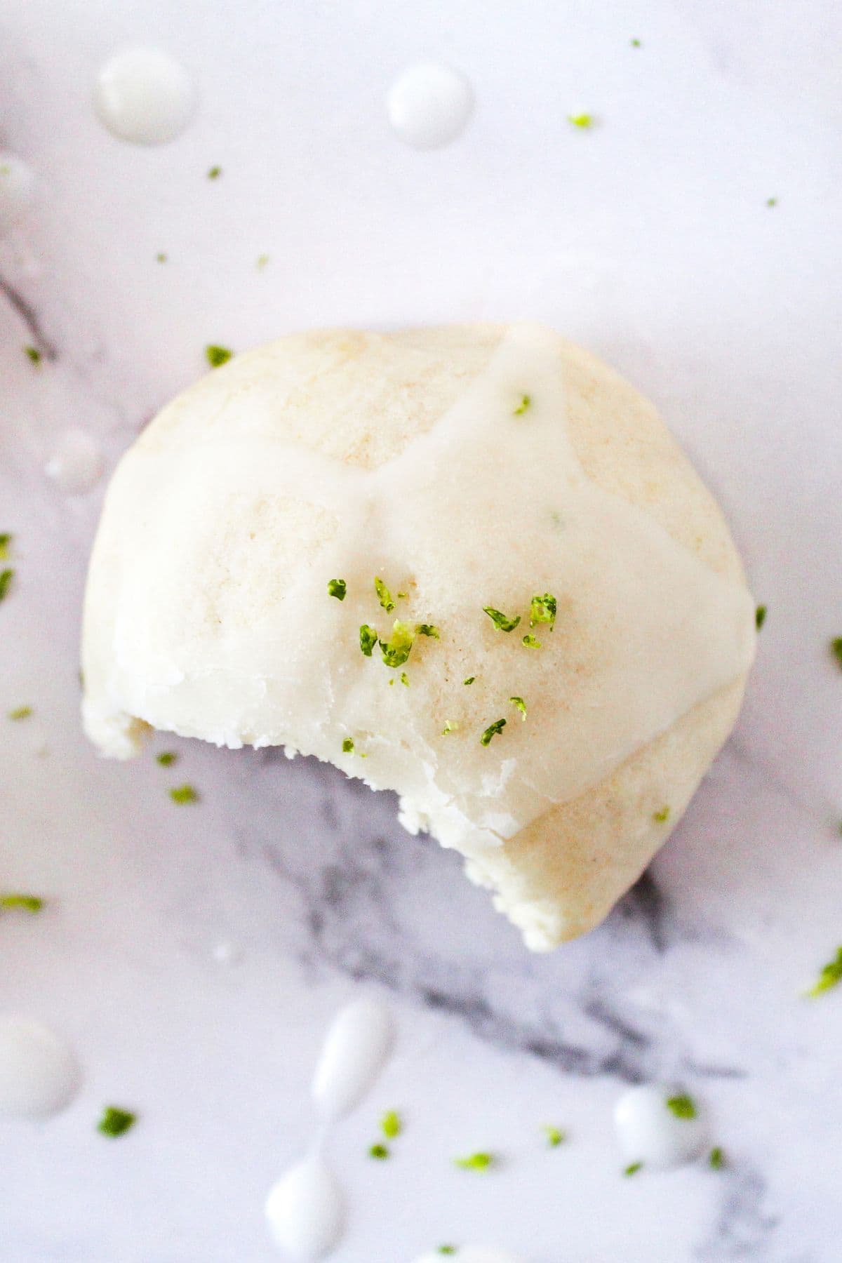 Delicious white chocolate truffle garnished with fresh lime zest on a white marble surface.
