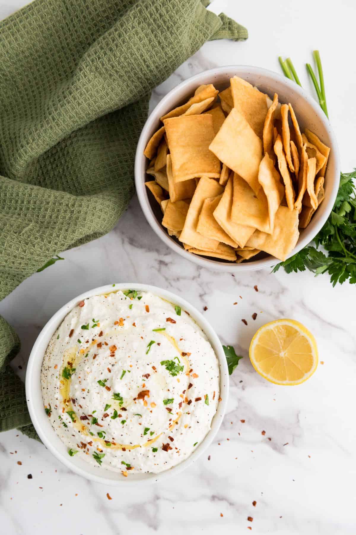 Healthy hummus dip served with crispy pita chips on a marble surface.
