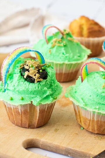 Colorful cupcakes with green frosting, rainbow candy, and festive sprinkles for St. Patrick's Day.