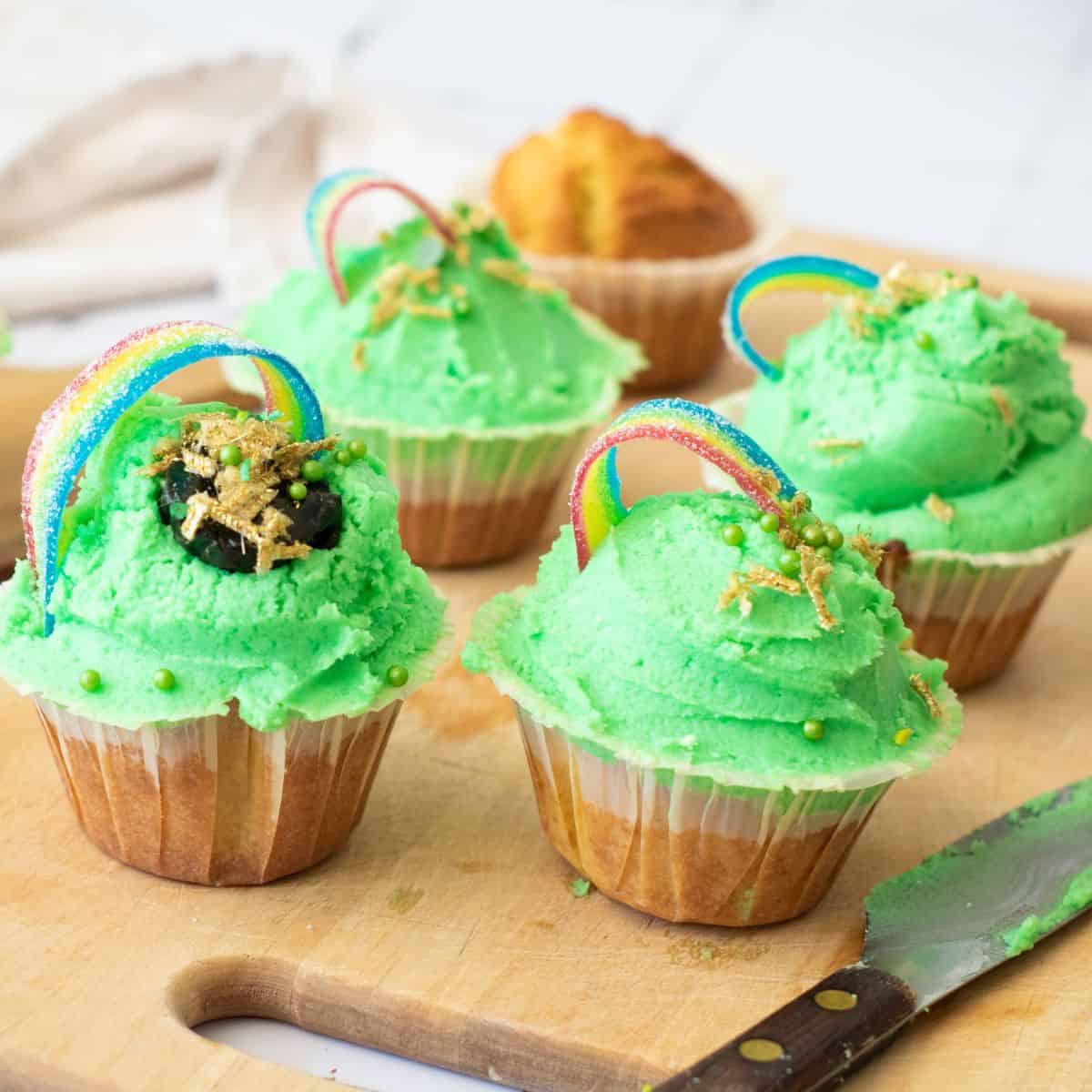 Colorful cupcakes with green frosting, rainbow candy, and festive sprinkles for St. Patrick's Day.